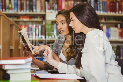 Student showing something to her classmate in the book