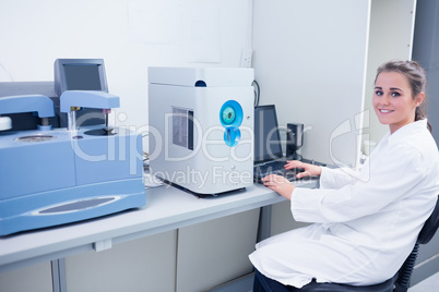 Smiling young biochemist using laptop at her desk