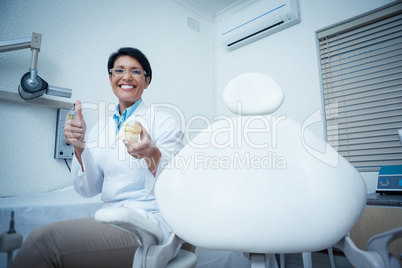 Dentist gesturing thumbs up while holding mouth model