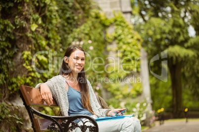 Smiling student sitting on bench holding her mobile phone