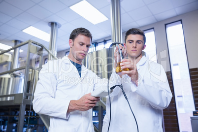 Two men in lab coat testing beer in the beaker