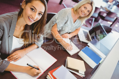 Smiling matures females students writing notes at desk