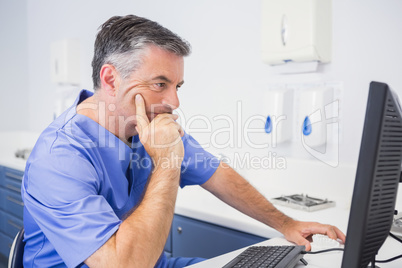 Serious dentist sitting and using computer