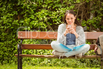 Smiling student sitting on bench text message on her mobile phon