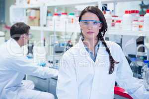 Unsmiling chemist standing in front of her colleague