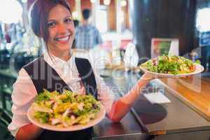 Pretty barmaid holding plates of salads