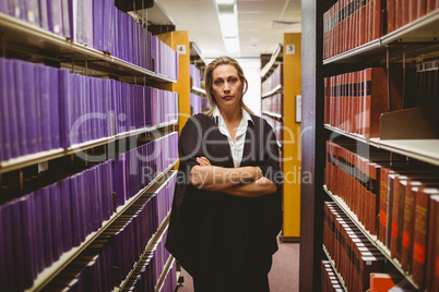 Unsmiling lawyer standing between shelfs with arms crossed