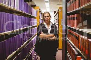 Unsmiling lawyer standing between shelfs with arms crossed