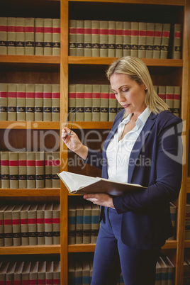 Focused librarian reading book and holding reading glasses