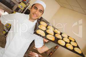 Baker smiling at camera holding tray of rolls