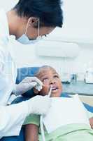 Female dentist examining boys teeth in dentists chair