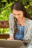 Smiling student sitting on bench listening music and using lapto