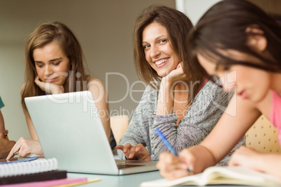 Smiling friends sitting studying and using laptop