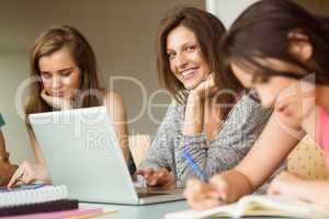 Smiling friends sitting studying and using laptop