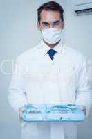 Male dentist in surgical mask holding tray of tools