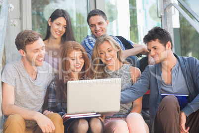 Happy students looking at laptop outside