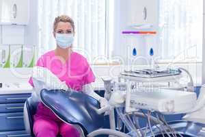 Dentist in pink scrubs looking at camera beside chair