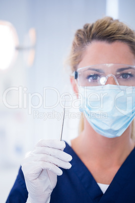 Dentist in mask holding dental explorer