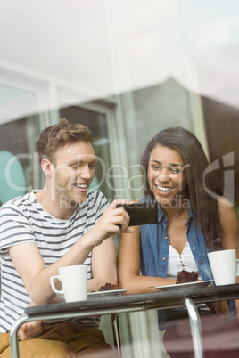 Smiling friends with chocolate cake using smartphone