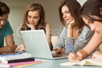 Smiling friends sitting studying and using laptop