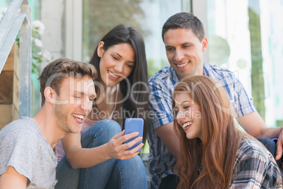 Happy students looking at smartphone outside on campus