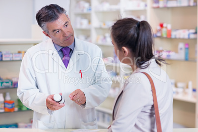 Pharmacist holding a bottle of drugs talking to customer