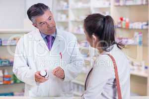 Pharmacist holding a bottle of drugs talking to customer