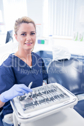 Dentist sitting with tray of tools smiling at camera