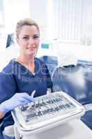 Dentist sitting with tray of tools smiling at camera