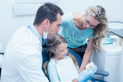 Dentist with assistant teaching girl how to brush teeth