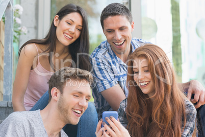 Happy students looking at smartphone outside on campus