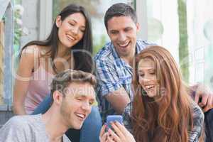 Happy students looking at smartphone outside on campus