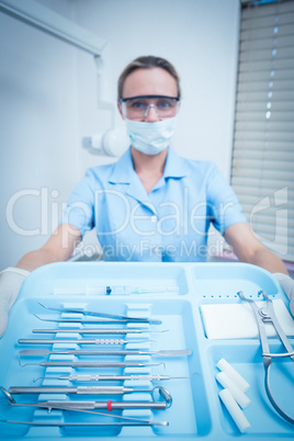Female dentist in surgical mask holding tray of tools