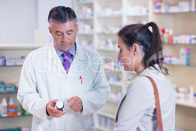 Pharmacist holding a bottle of drugs talking to customer