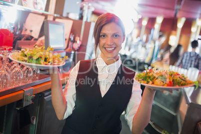 Pretty barmaid holding plates of salads