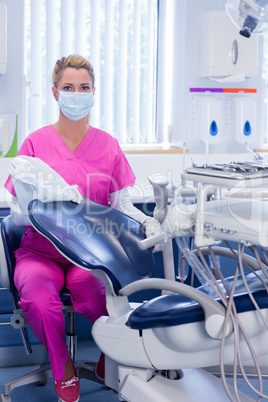 Dentist in pink scrubs looking at camera beside chair