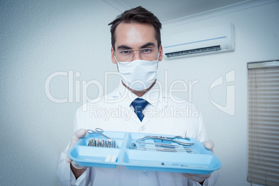 Male dentist in surgical mask holding tray of tools