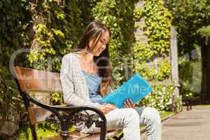 Smiling student sitting on bench and reading book