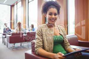 Student sitting on sofa using her tablet pc smiling at camera