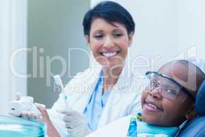 Female dentist teaching boy how to brush teeth