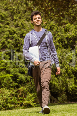 Student walking with shoulder bag and holding notepad