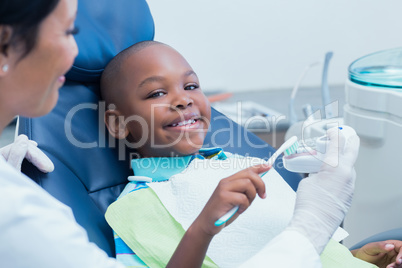 Dentist teaching happy boy how to brush teeth