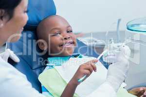 Dentist teaching happy boy how to brush teeth