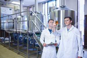 Two men in lab coat looking at the beaker with beer