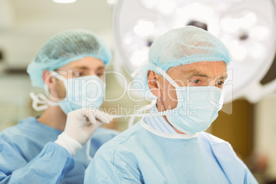 Young surgeon tying older surgeons mask