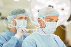 Young surgeon tying older surgeons mask