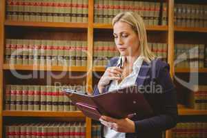 Thinking female librarian holding textbook