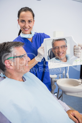 Smiling dentist showing teeth of her patient with a mirror