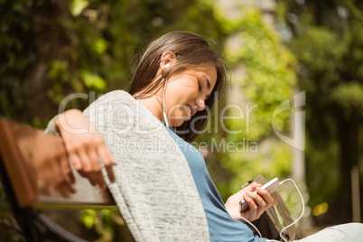 Smiling student sitting on bench text message on her mobile phon