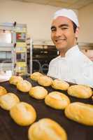 Baker smiling at camera holding tray of rolls